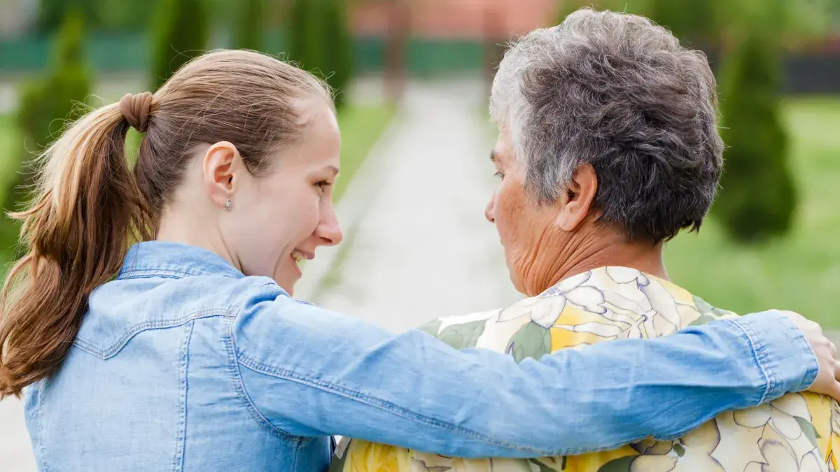 Photo of younger woman in blue shirt embracing older woman in floral shirt
