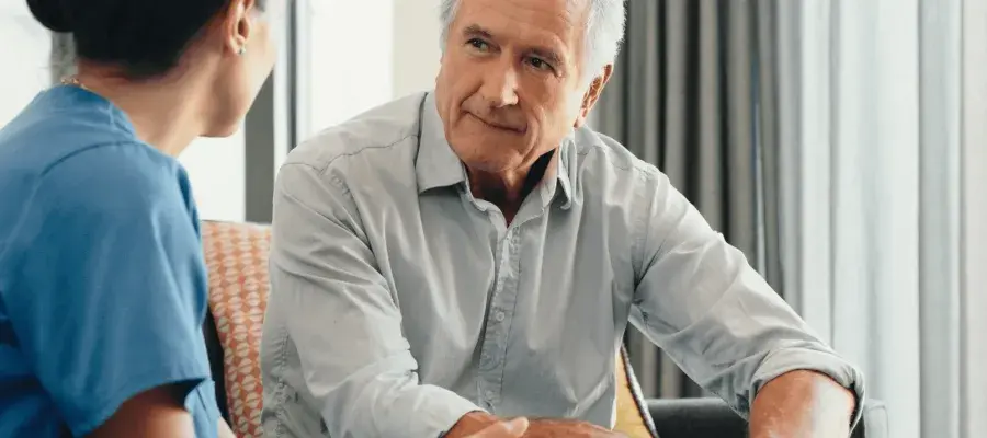 A nurse with dark hair speaks to an elderly man.