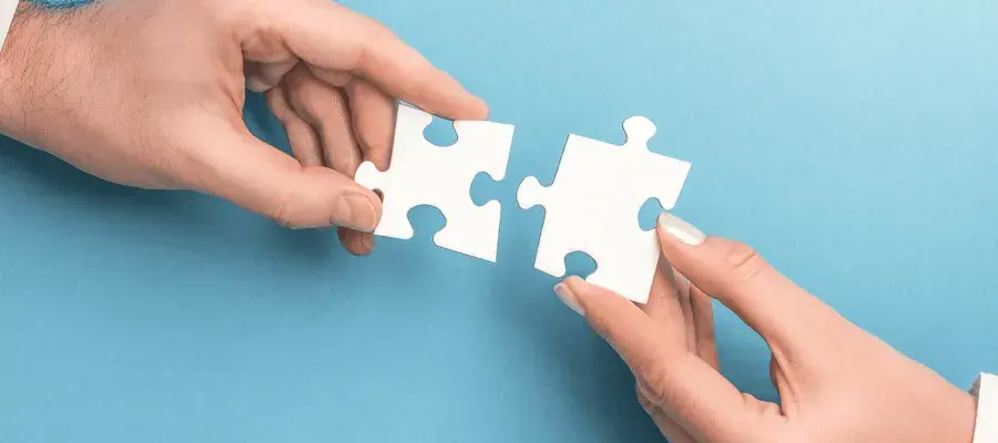 Blue background, two hands holding white jigsaw pieces