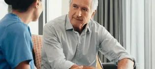 A nurse with dark hair speaks to an elderly man.