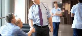 A man in a shirt and tie shaking the hand of another man who is sitting down on a couch