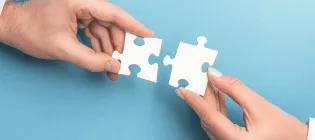 Blue background, two hands holding white jigsaw pieces